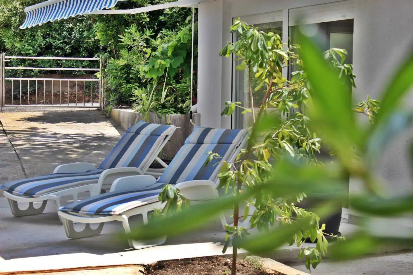 Terrazza in giardino dell'Apartment con due lettini a righe sotto una tenda da sole