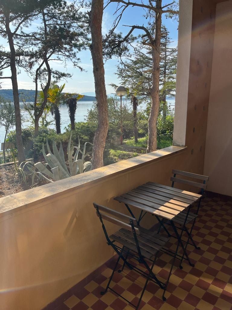 Balcone con un tavolino e due sedie, con vista sul mare tra i pini