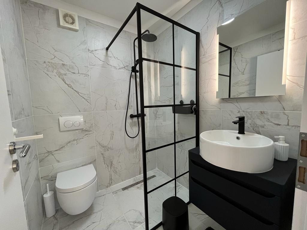Bagno con piastrelle bianche effetto marmo e doccia walk-in con profili neri