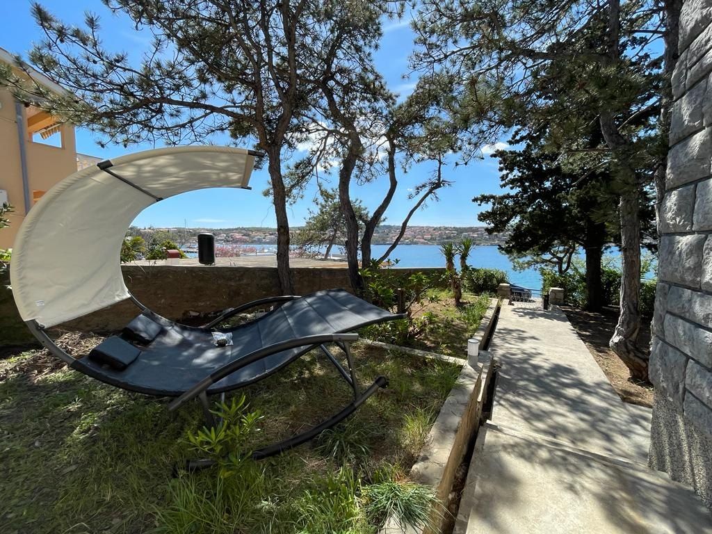 Giardino con una poltrona sospesa sotto i pini e il mare della baia