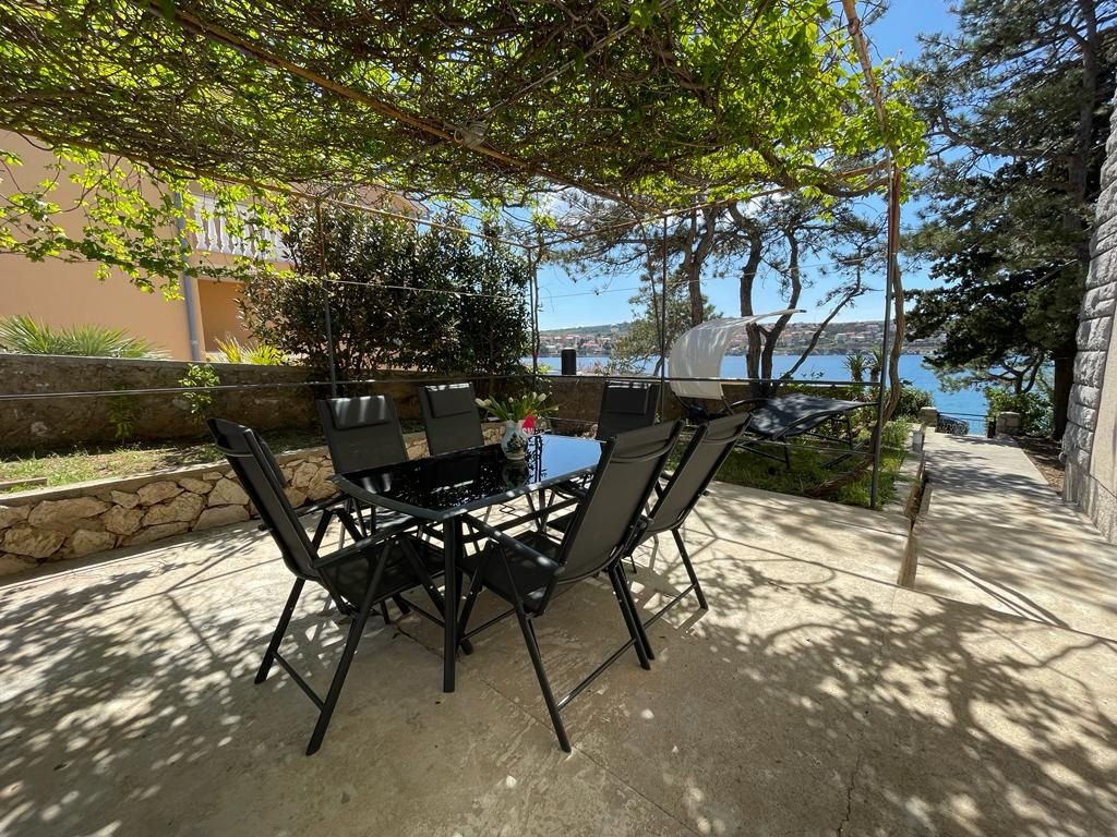 Terrazza della BeachHouse con un tavolo da pranzo e sei sedie sotto un pergolato di vite, con la baia di Šilo sullo sfondo